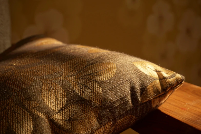 a brown pillow sitting on top of a wooden chair, a macro photograph, inspired by Alexandre Cabanel, arts and crafts movement, gold leaves, luminescent fabrics, brown and gold, product shot