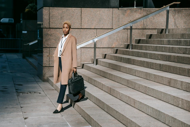 a woman standing on the steps of a building, by Carey Morris, pexels contest winner, trench coat and suit, work clothes, black female, bag over the waist