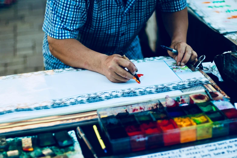 a man sitting at a table writing on a piece of paper, a watercolor painting, pexels contest winner, crafts and souvenirs, indi creates, intricately defined, painted overalls