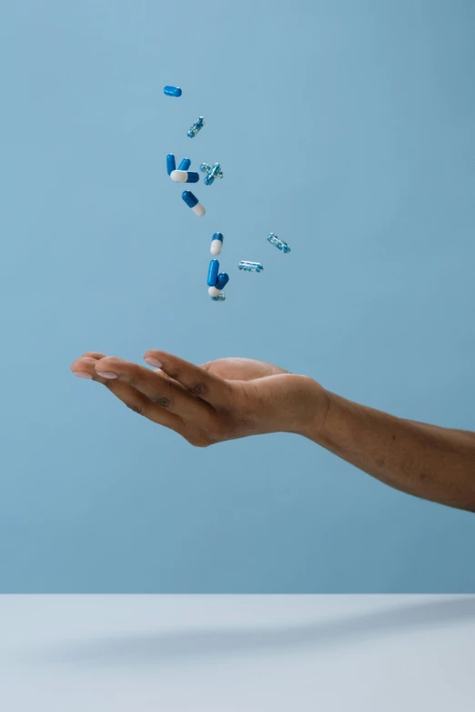 a person holding a bunch of pills in their hand, by Sebastian Vrancx, pexels, hyperrealism, blue, arms extended, multiple stories, hovering indecision