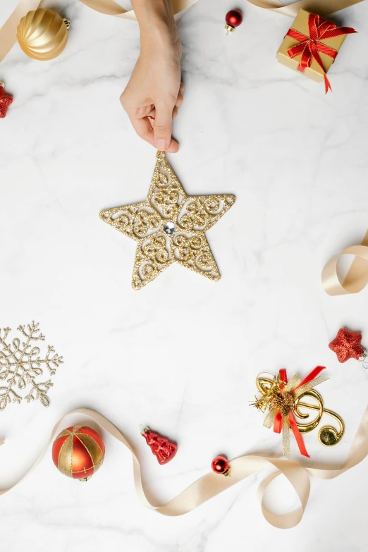 a person holding a star ornament surrounded by christmas decorations, arabesque, flatlay, profile image, premium, marble and gold