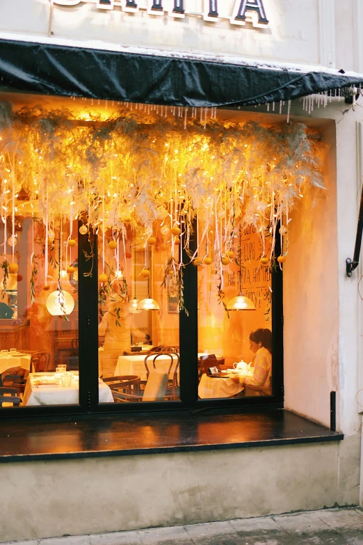 a woman walking down a street past a store front, inspired by Eva Gonzalès, art nouveau, covered in flame porcelain vine, floating lights, white and gold color scheme, the window is open