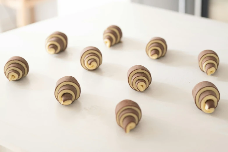 a table topped with lots of chocolate covered doughnuts, inspired by Károly Patkó, op art, cyber copper spiral decorations, natural wood top, set against a white background, on grey background