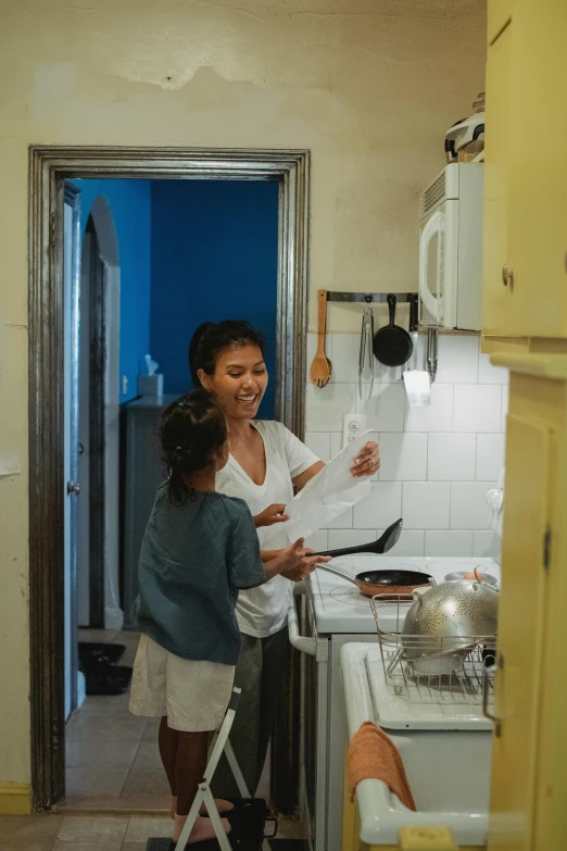 a woman standing in a kitchen next to a stove, woman holding another woman, joy ang, blue print, still frame