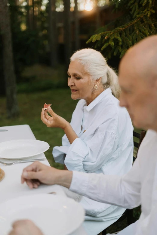 a group of people sitting around a table eating food, white haired lady, nature outside, profile image, couple