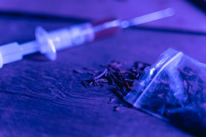 a syll sitting on top of a table next to a syll, by Adam Marczyński, unsplash, process art, drugs, blue and purple, holding a syringe, crime scene photo