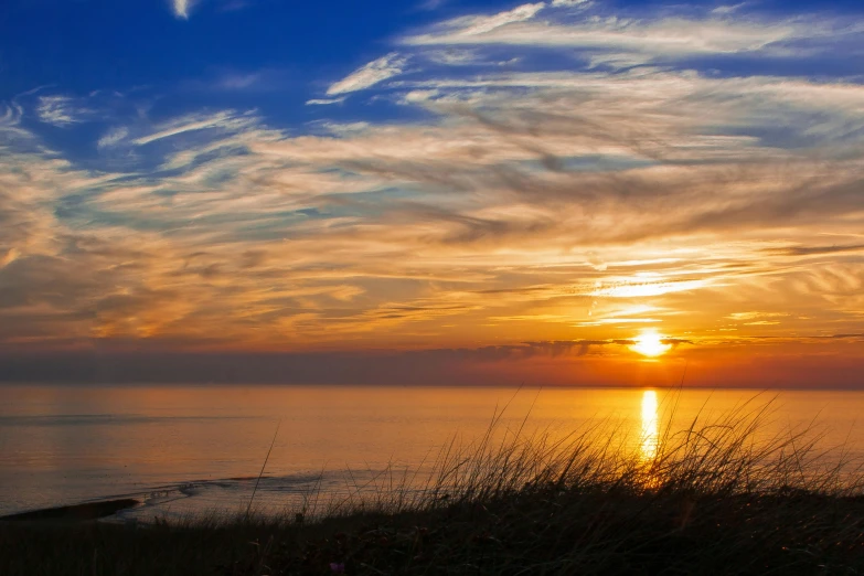 the sun is setting over a body of water, by Jan Tengnagel, pexels contest winner, omaha beach, sunset panorama, thumbnail, standing in the grass at sunset