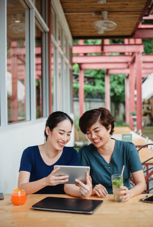 two women sitting at a table looking at a tablet, pexels contest winner, south east asian with long, delightful, outside, 64x64