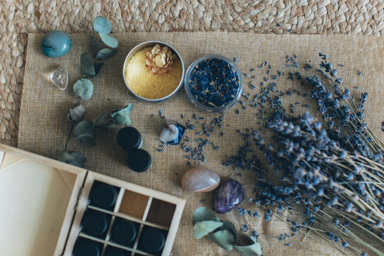 a box sitting on top of a table next to a bunch of flowers, trending on pexels, process art, dried herbs, gold and cobalt tiles, skin care, black and blue and purple scheme