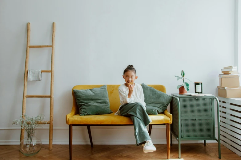 a woman sitting on top of a yellow couch, pexels contest winner, minimalism, 4yr old, young asian girl, french provincial furniture, on a white table