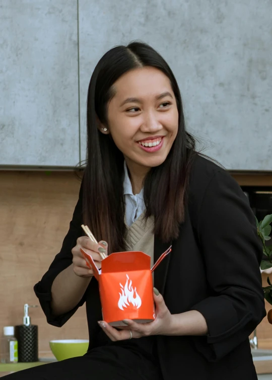 a woman sitting on a kitchen counter holding a bowl of food, inspired by Feng Zhu, fire and flames, serving happy meals, engineer, headshot profile picture