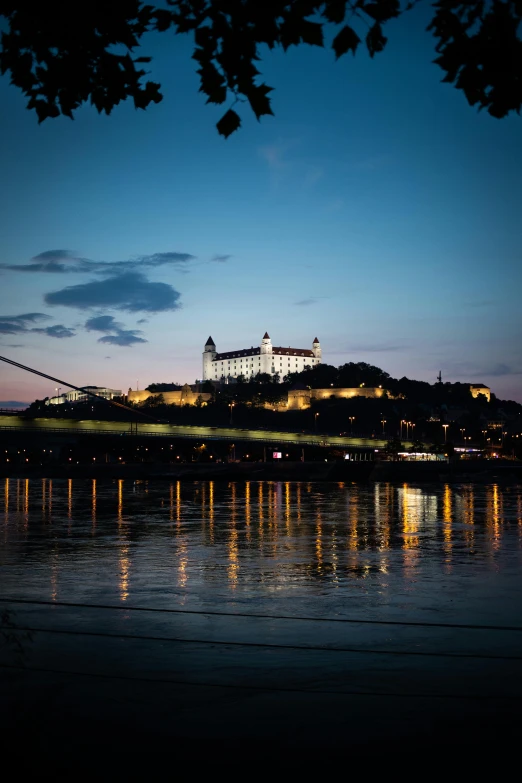 a castle sitting on top of a hill next to a river, city lights in the background, trams, sk, color photo