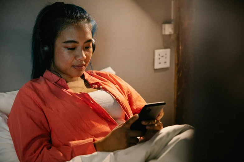 a woman sitting on a bed using a cell phone, wearing black headphones, everything fits on the screen, multiple stories, an asian woman
