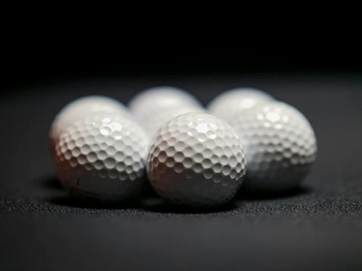 a group of golf balls sitting on top of a black surface, in front of a round, high quality product image”, looking towards camera, thumbnail