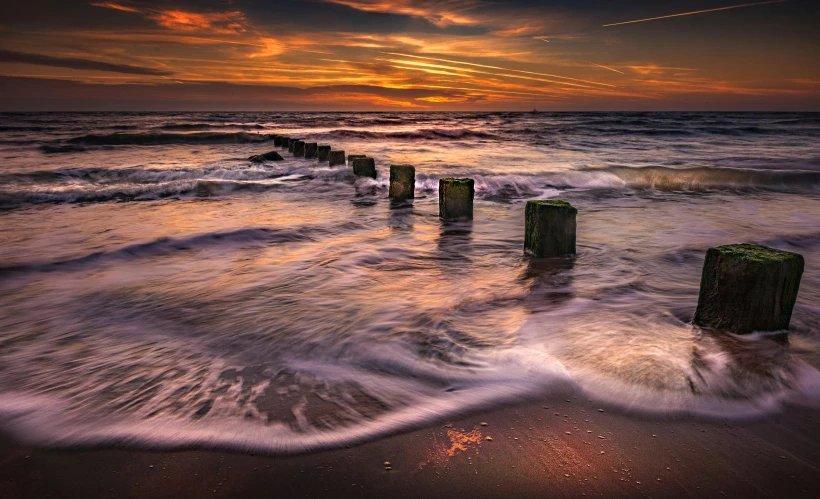 a sunset over the ocean with wooden posts sticking out of the water, by Andries Stock, pexels contest winner, sea waves, sandy colors, turbulent sea, today\'s featured photograph 4k