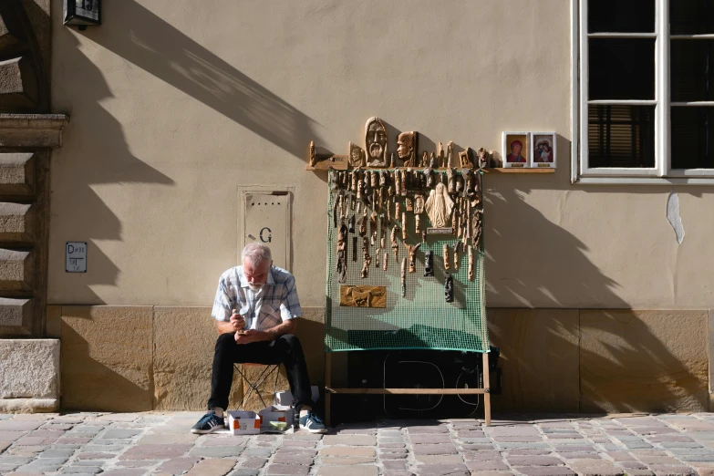 a man sitting on a bench in front of a building, pexels contest winner, temporary art, selling his wares, gilding, pekka halonen, wind chimes