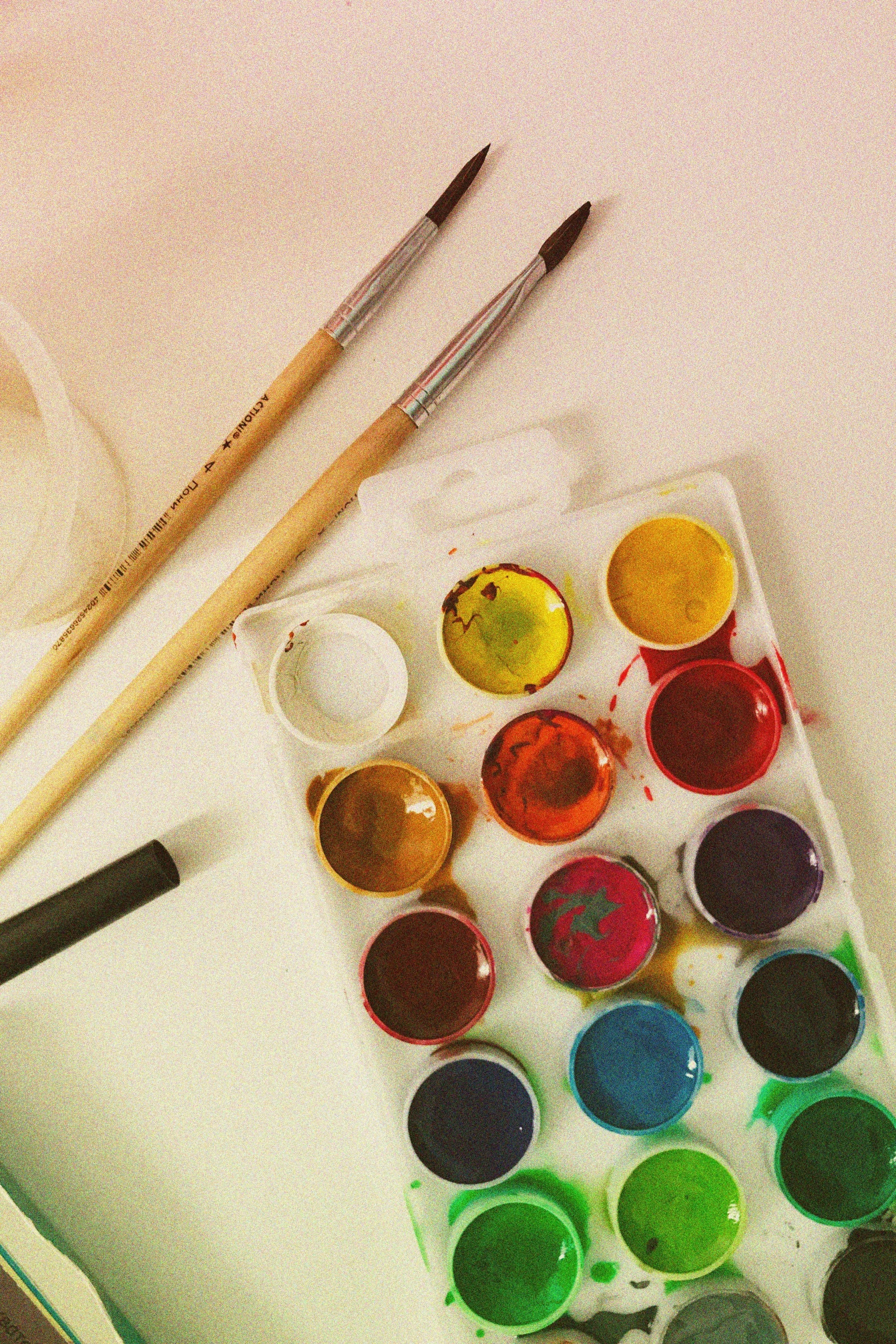 a close up of paint and brushes on a table, a watercolor painting, inspired by artist, pexels, art & language, flat lay, multicoloured, video, crafts