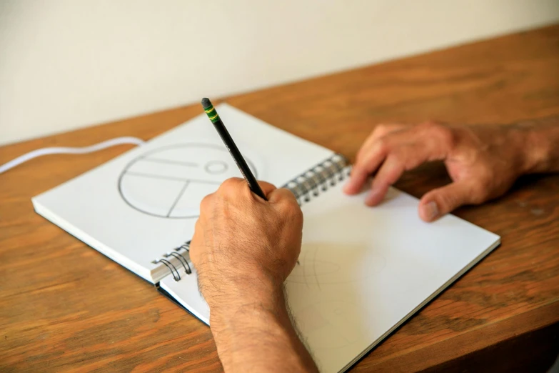 a person writing on a notebook with a pencil, a drawing, proportions on a circle, back of hand on the table, black pen drawn edges, caran d'ache luminance