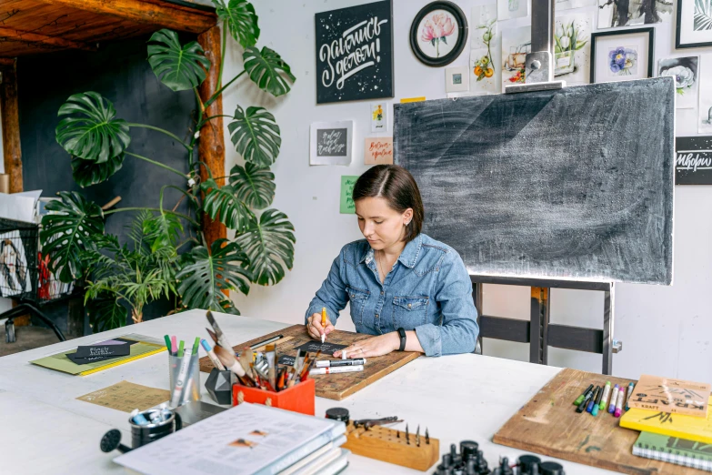 a woman sitting at a table working on a project, a woodcut, trending on unsplash, anna nikonova aka newmilky, calligraphy, studio shot, in a classroom