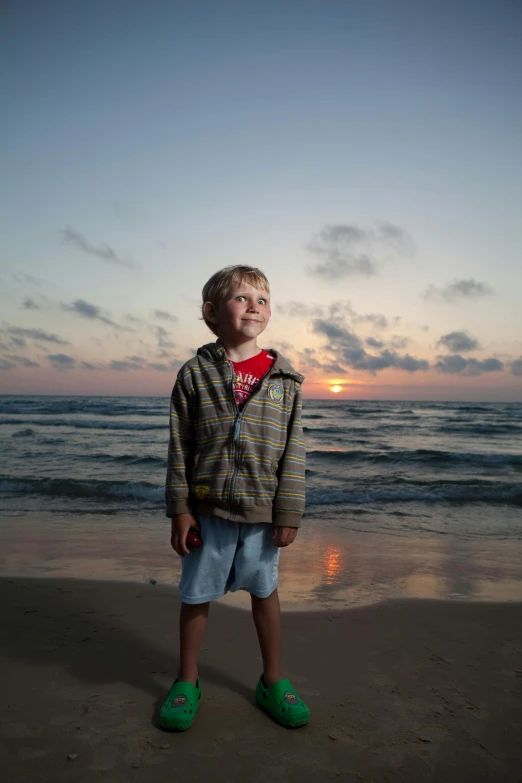 a young boy standing on top of a sandy beach, by Michael Goldberg, sunset lighting, standing beside the ocean, blond boy, taken in the late 2010s