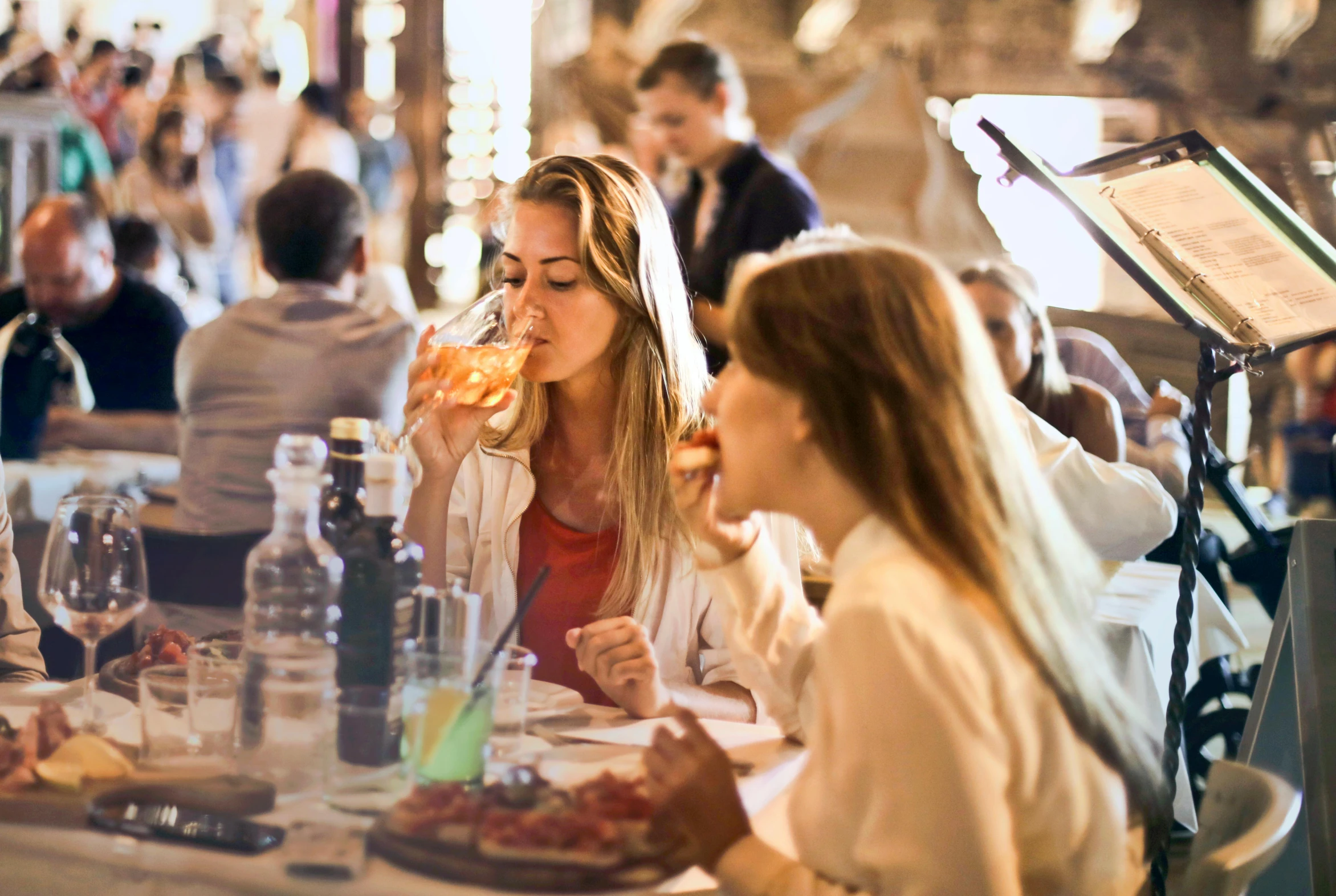 a group of people sitting at a table eating pizza, profile image, blonde, drinking, urban surroundings