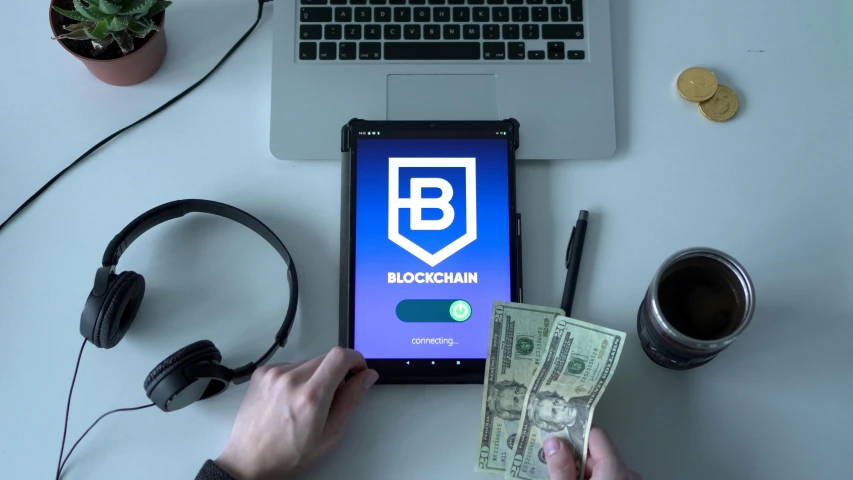 a cell phone sitting on top of a table next to a laptop, blockchain vault, banknote, a person standing in front of a, promo image