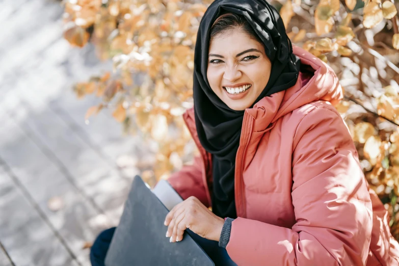 a woman sitting on a bench with a laptop, pexels contest winner, hurufiyya, wearing a turtleneck and jacket, welcoming grin, wearing a head scarf, at college