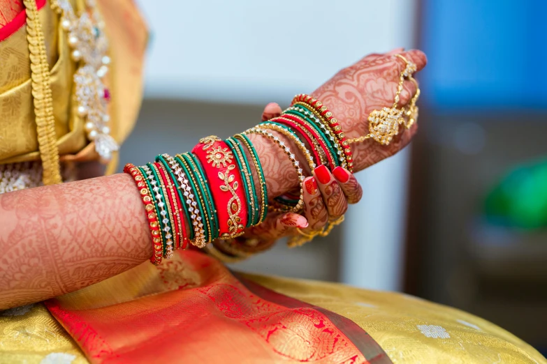 a close up of a woman's hands with bracelets, pexels, hurufiyya, wearing sari, red and green, wedding, multicoloured