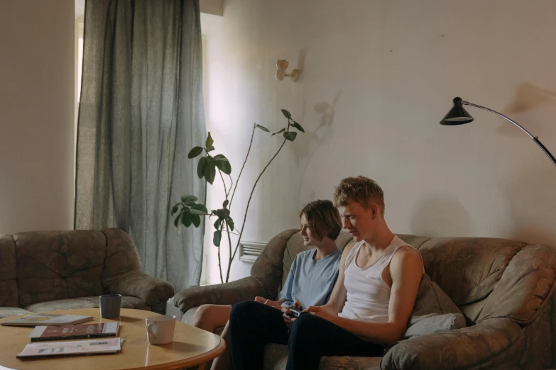 two people sitting on a couch in a living room, unsplash, hyperrealism, movie footage, teenage boy, ignant, summer afternoon