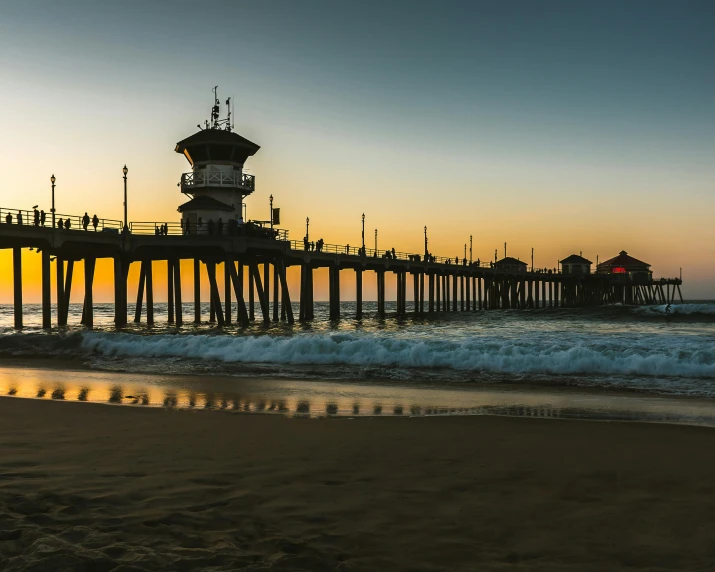 a pier sitting on top of a sandy beach next to the ocean, by Jacob Burck, unsplash contest winner, renaissance, southern california, square, light house, on the beach during sunset