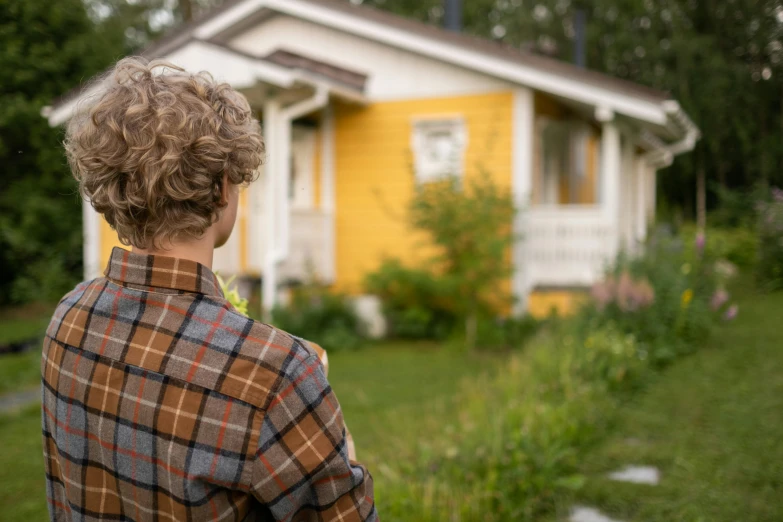 a woman standing in front of a yellow house, by Jaakko Mattila, shutterstock, close-up shot taken from behind, cottage close up, tv show still, settlement