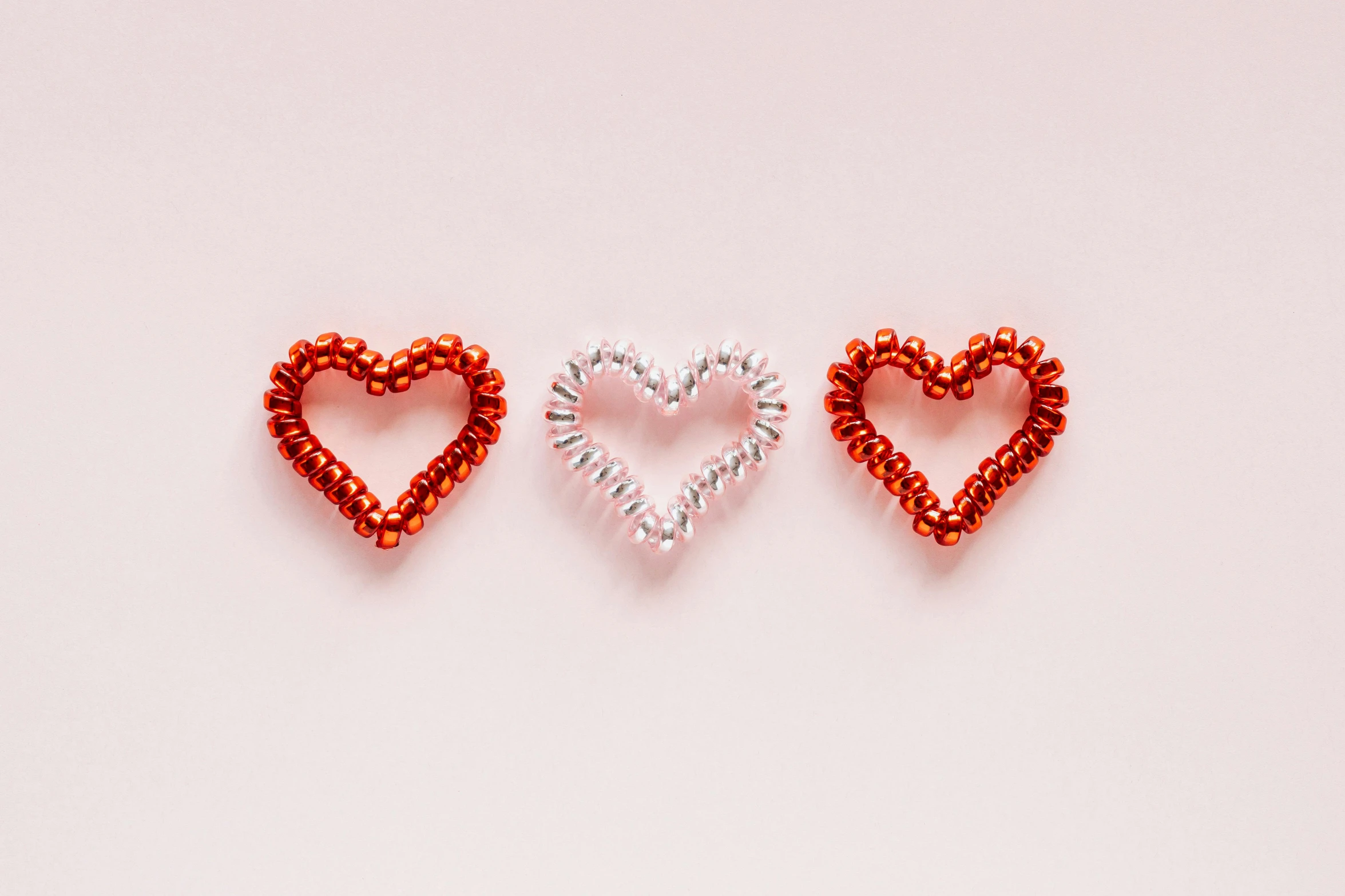 three red beaded hearts on a white background, an album cover, pexels, coral red, silver, thumbnail, pink