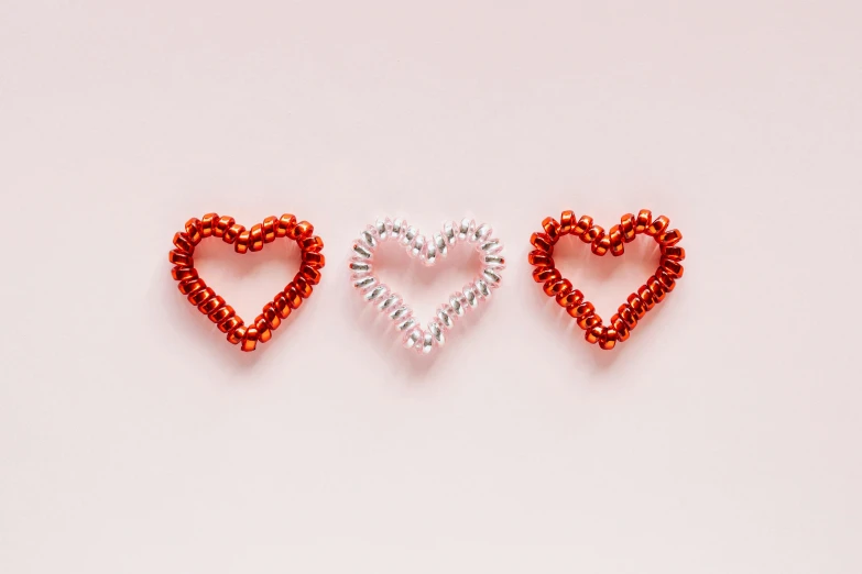 three red beaded hearts on a white background, an album cover, pexels, coral red, silver, thumbnail, pink