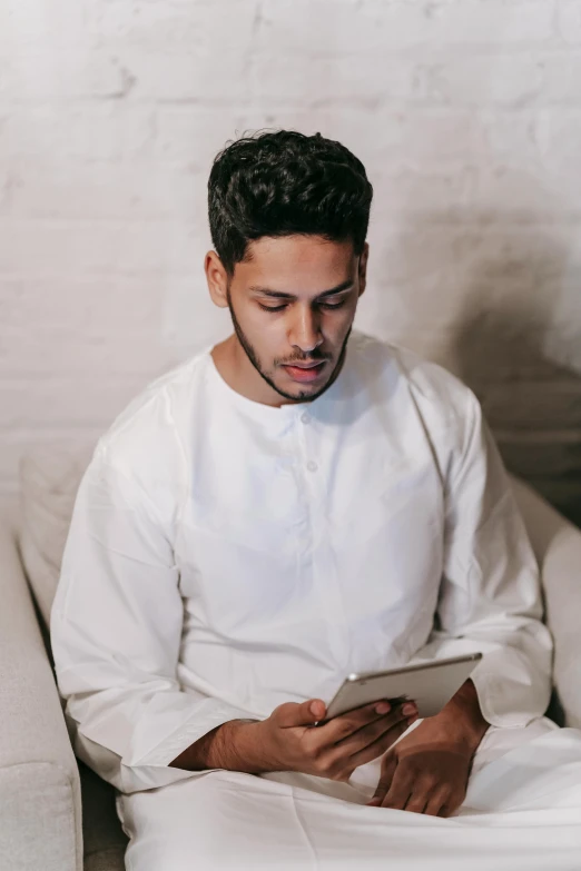 a man sitting on a couch using a tablet, inspired by Ahmed Yacoubi, pexels contest winner, hurufiyya, white dress shirt, looking serious, gif, arabian