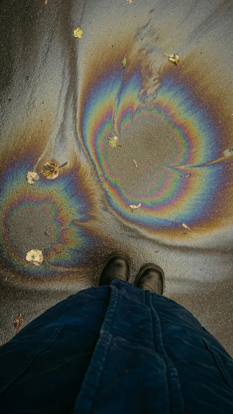 a person standing in front of a puddle of oil, inspired by Gabriel Dawe, trending on pexels, oil spills, muted rainbow tubing, sidewalk, snapchat photo