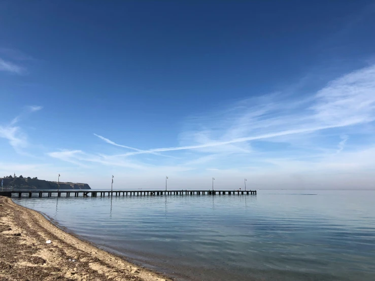 a large body of water next to a beach, by Niko Henrichon, near a jetty, blue sky, 8k octan photo, # nofilter