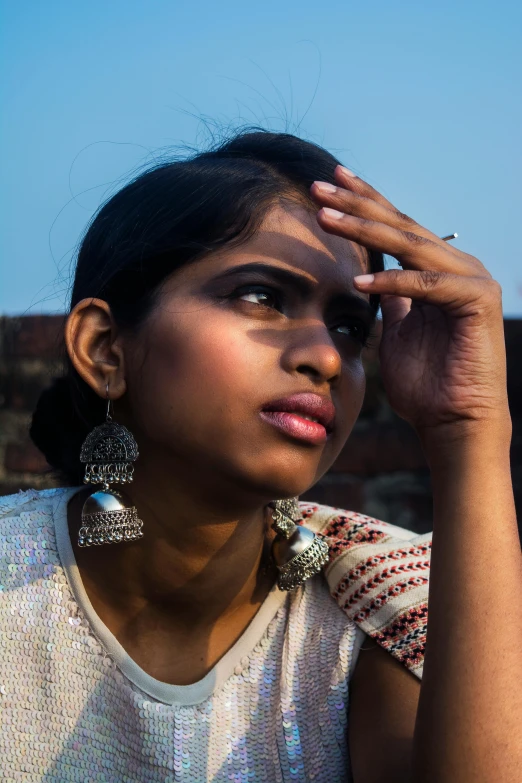 a close up of a person holding a cell phone, bengal school of art, big earrings, pensive and hopeful expression, sunlit sky, hindu aesthetic