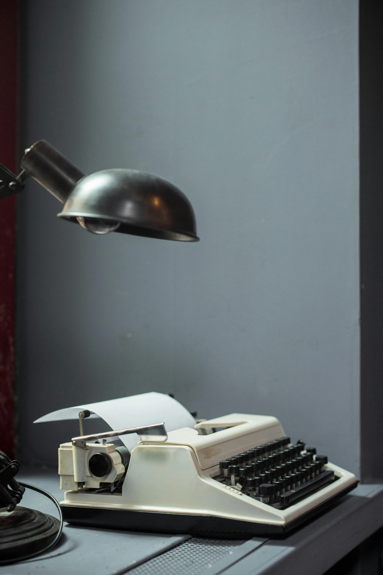 an old typewriter sitting on a desk next to a lamp, inspired by Otto Stark, lightbox, frontal shot, grey, panel