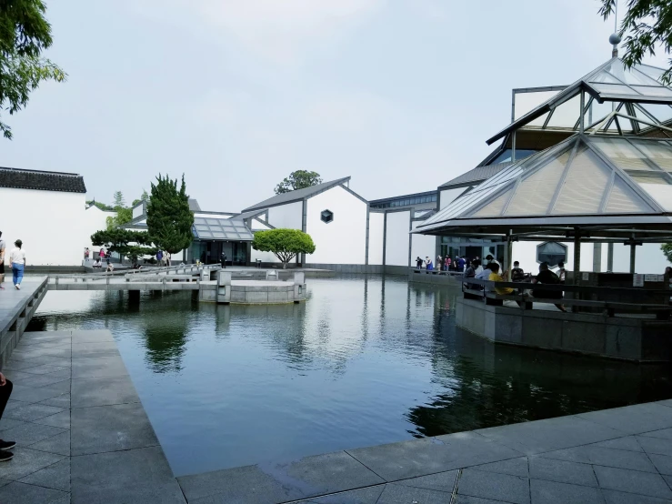 a pond filled with lots of water next to a building, by Cheng Jiasui, house's and shops and buildings, exterior view, museum photo, grey