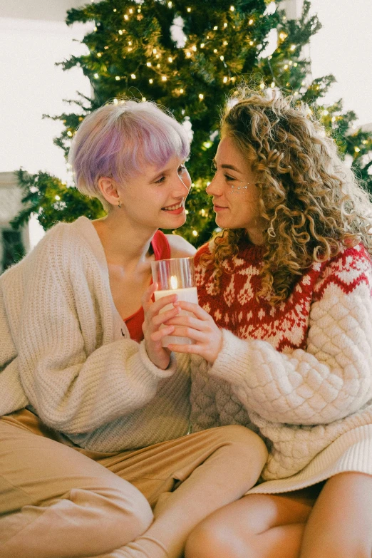 a couple of women sitting on top of a bed next to a christmas tree, trending on pexels, renaissance, drink milkshakes together, lilac hair, holding hands, lesbian