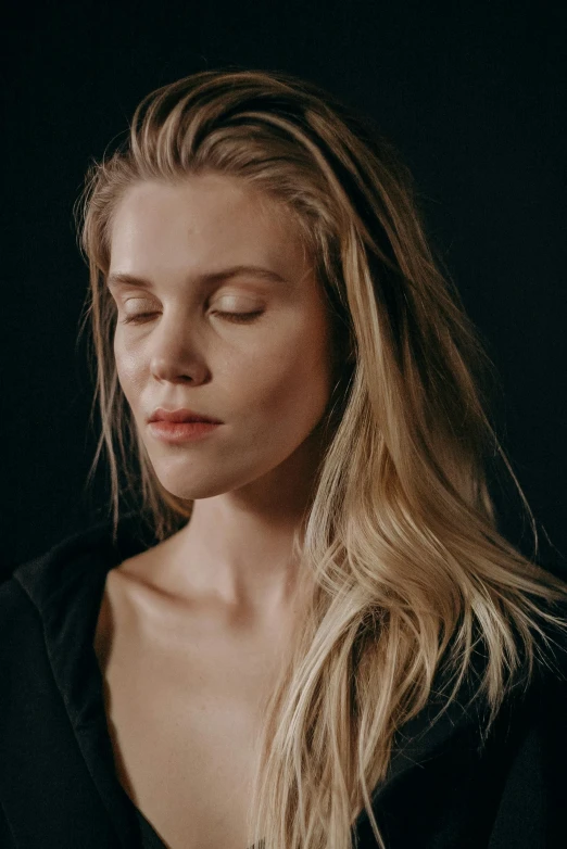 a woman with long blonde hair standing in front of a black background, symmetrical face orelsan, eyes closed, contemplative, person in foreground