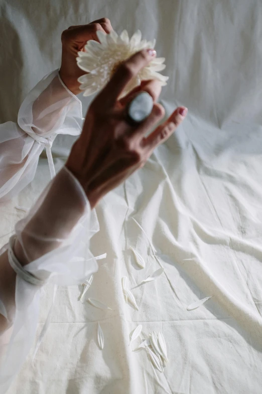 a woman in a white dress holding a flower, by Rebecca Horn, unsplash, renaissance, flowing silk sheets, white bandage tape on fists, photograph from above, sheer fabrics