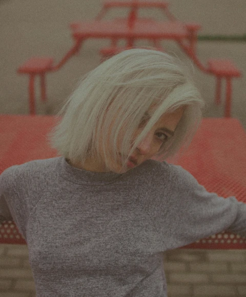 a woman standing in front of a red table, an album cover, inspired by Elsa Bleda, pexels contest winner, realism, with short bobbed white hair, sitting on a park bench, teenage girl, slightly smirking