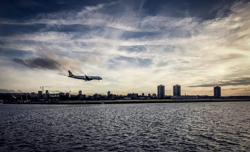 a large jetliner flying over a body of water, by Carey Morris, pexels contest winner, hurufiyya, canary wharf, shoreline, fujifilm”