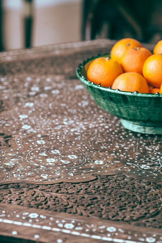 a bowl of oranges sitting on a table, inspired by Riad Beyrouti, trending on unsplash, arts and crafts movement, intricate penwork, hand carved brown resin, detail shot, tablecloth