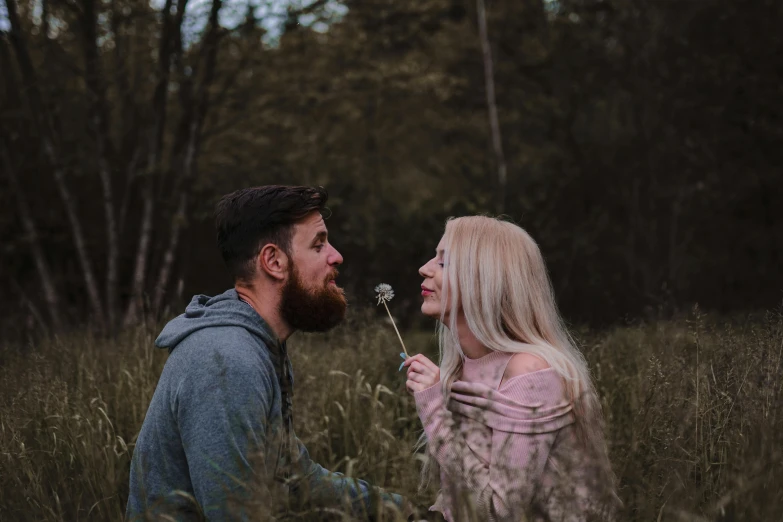 a man and a woman sitting in a field of tall grass, by Adam Marczyński, pexels contest winner, bearded, holding a flower, avatar image, grey