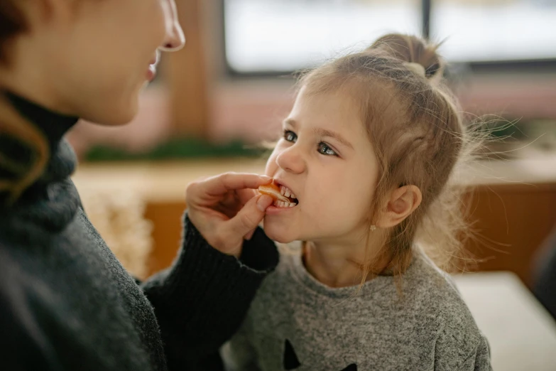 a woman feeding a little girl a piece of pizza, by Emma Andijewska, pexels contest winner, cute bandaid on nose!!, manuka, serving fries, schools