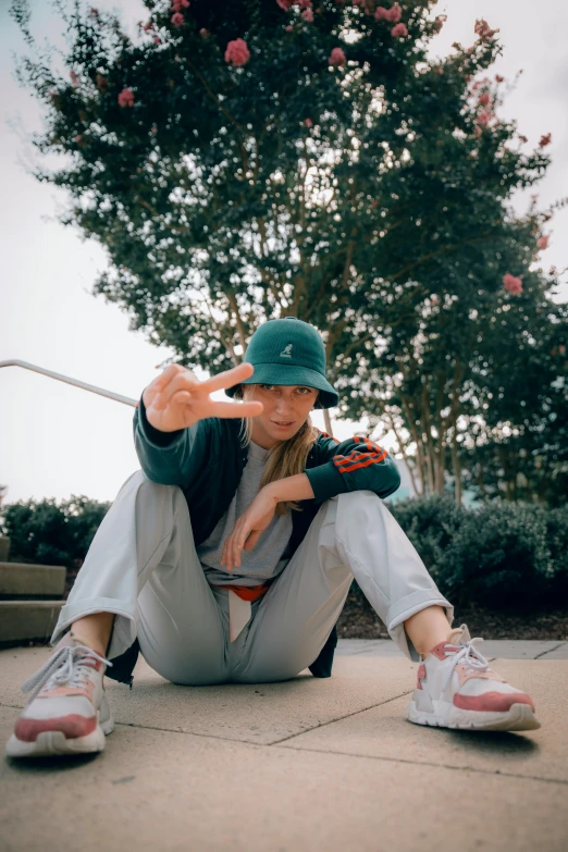 a person sitting on the ground with a skateboard, green hat, striking a pose, wearing a baseball hat, wearing a fisher 🧥