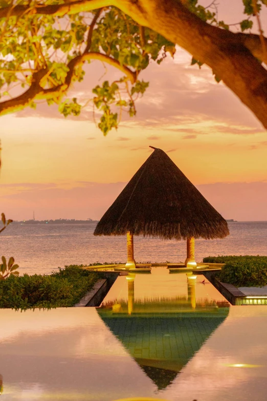 a gazebo sitting on top of a lush green field next to a body of water, maldives in background, sunset, slide show, sitting at the edge of pool