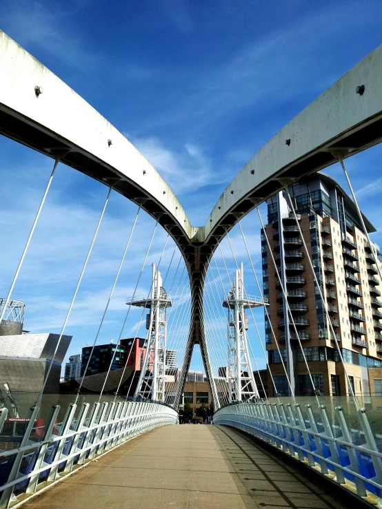 a close up of a bridge with buildings in the background, inspired by Zaha Hadid, pexels contest winner, manchester, thumbnail, walking towards camera, two organic looking towers